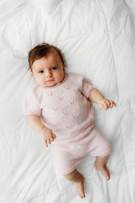 A baby wearing light pink short sleeves and shorts.
