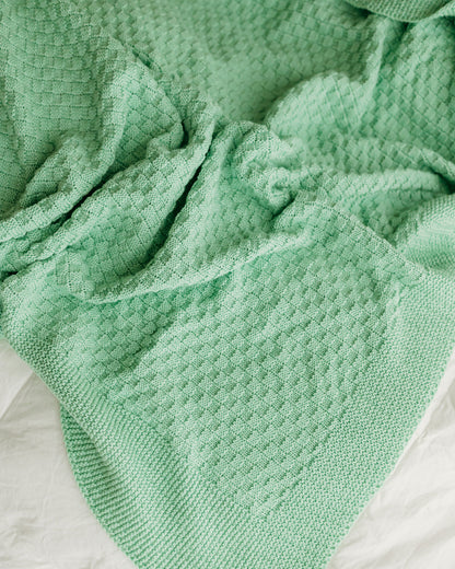 A soft, mint-green knitted blanket with a textured pattern.