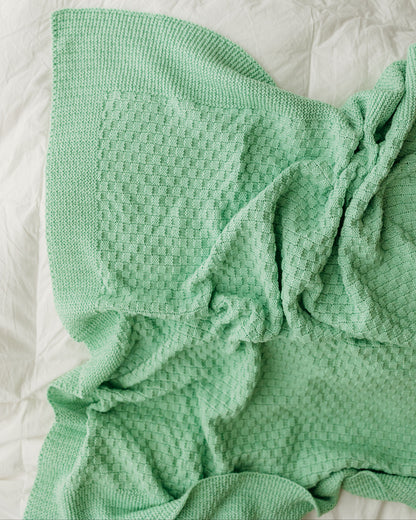 A mint-green blanket crumpled on a white sheet.