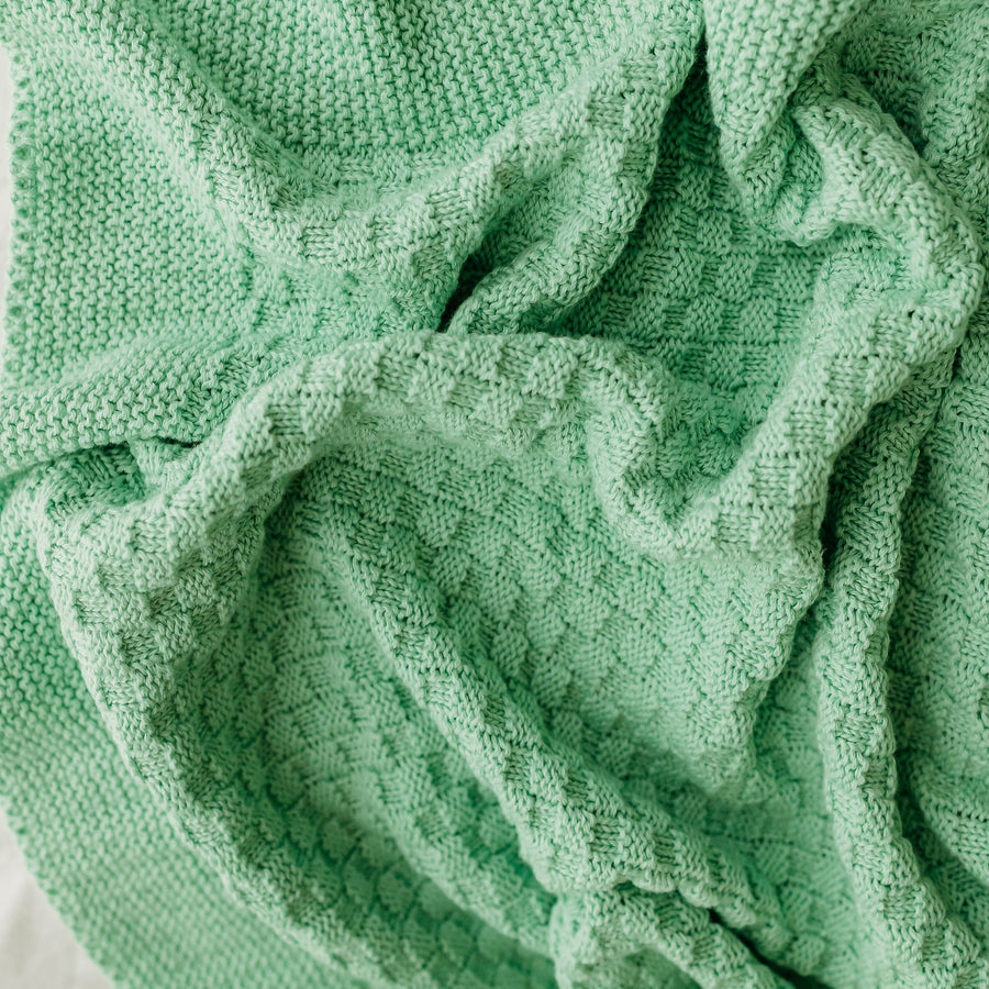 A textured mint green blanket with knitting patterns.