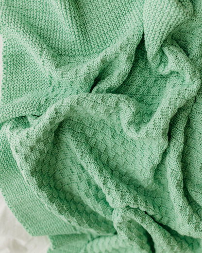 A textured mint green blanket with knitting patterns.