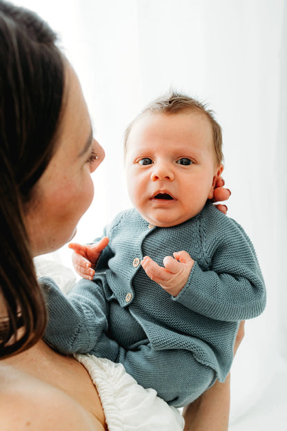 A woman lovingly holds a baby in a blue knitted onesie.