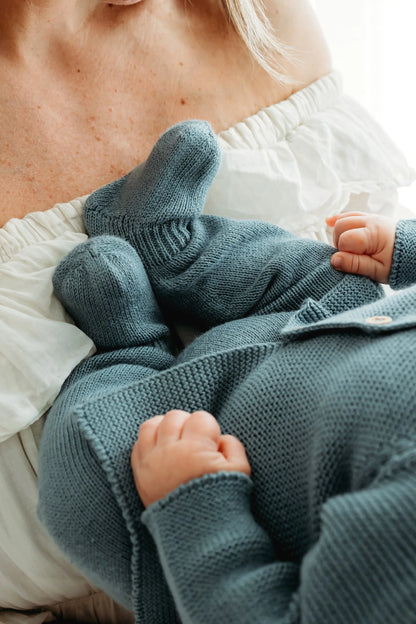 A baby in a knitted blue outfit is cradled by a woman.