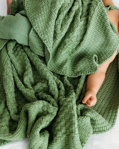 A baby is partially covered by a soft green knitted blanket.