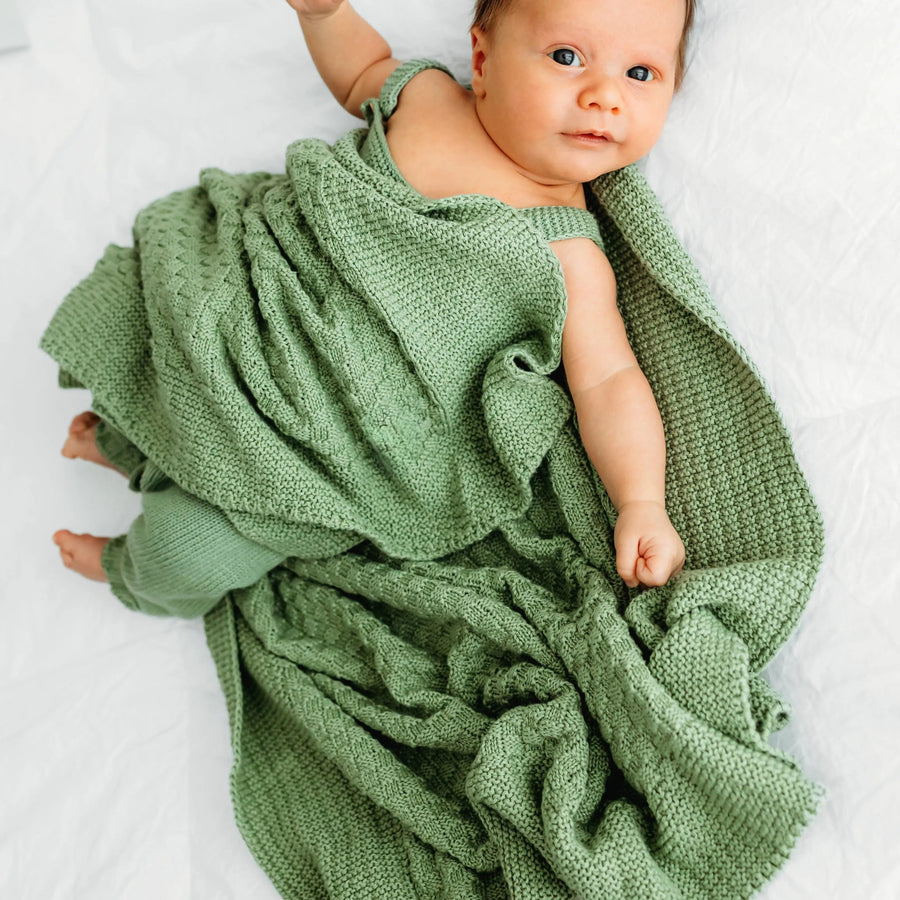 A baby on a white blanket, wrapped in a green blanket.