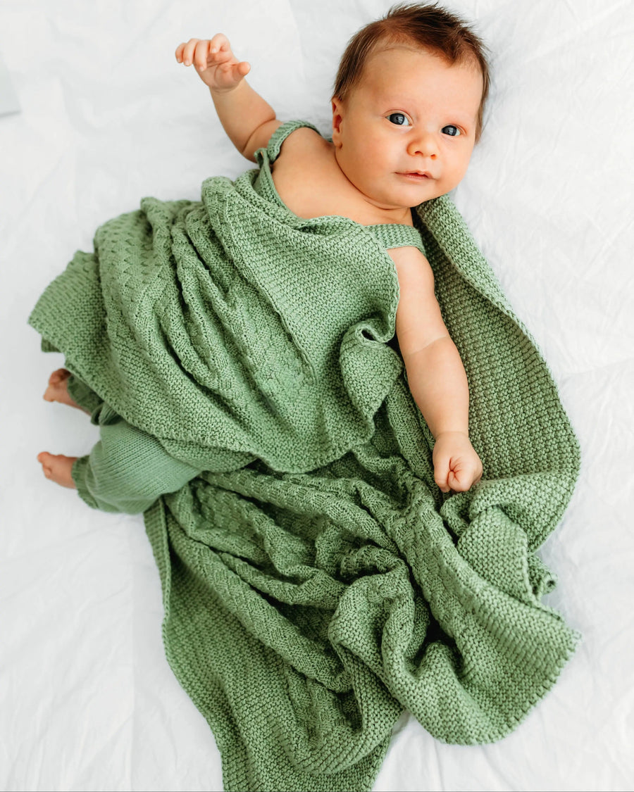 A baby on a white blanket, wrapped in a green blanket.