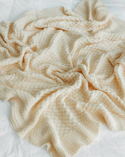 Cream-colored textured blanket crumpled on a white bedsheet.