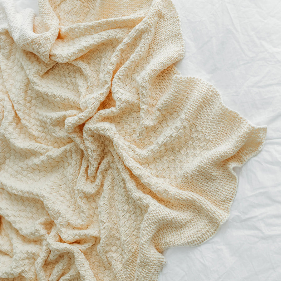 A crumpled beige textured blanket lies on a bedspread.