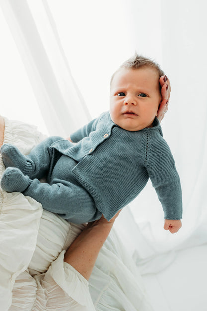 A baby in a blue knit outfit is held up by a woman.