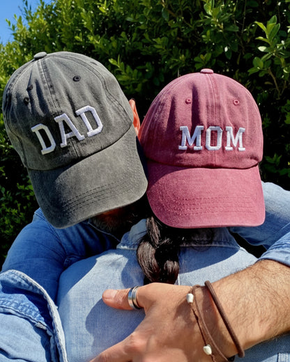 A couple wearing Dad and Mom caps are hugging each other.