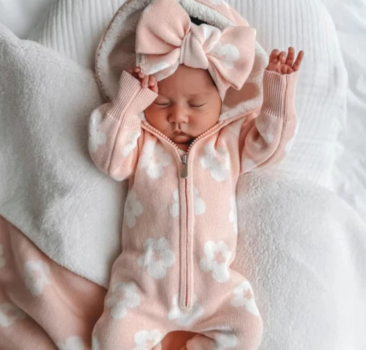 A baby in a peach floral onesie with a large matching bow.